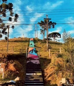 Escadaria pública de Jaquirana pintada em faixas de cor, vista de baixo, com o céu ao fundo