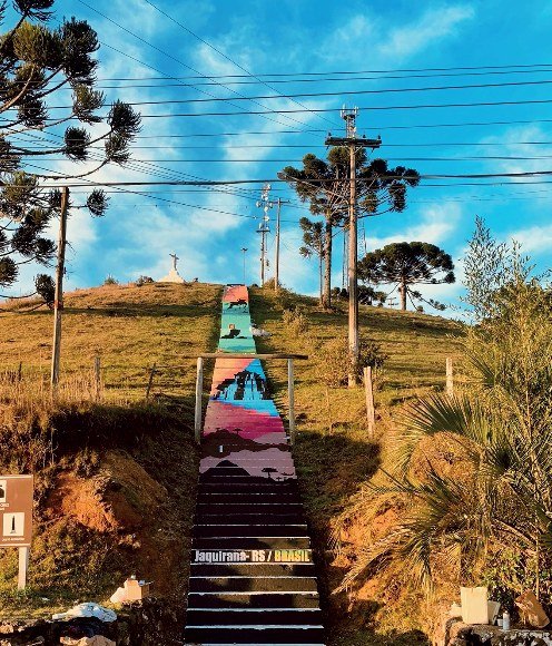 Escadaria pública de Jaquirana pintada em faixas de cor, vista de baixo, com o céu ao fundo